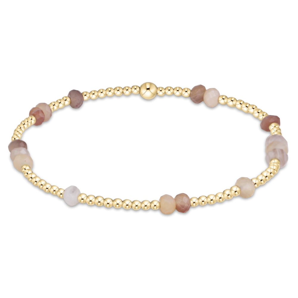 A delicate beaded bracelet with small gold-toned round beads and larger smooth stone-like beads in soft taupe, blush pink, and pale lavender, arranged in an oval on a white background.