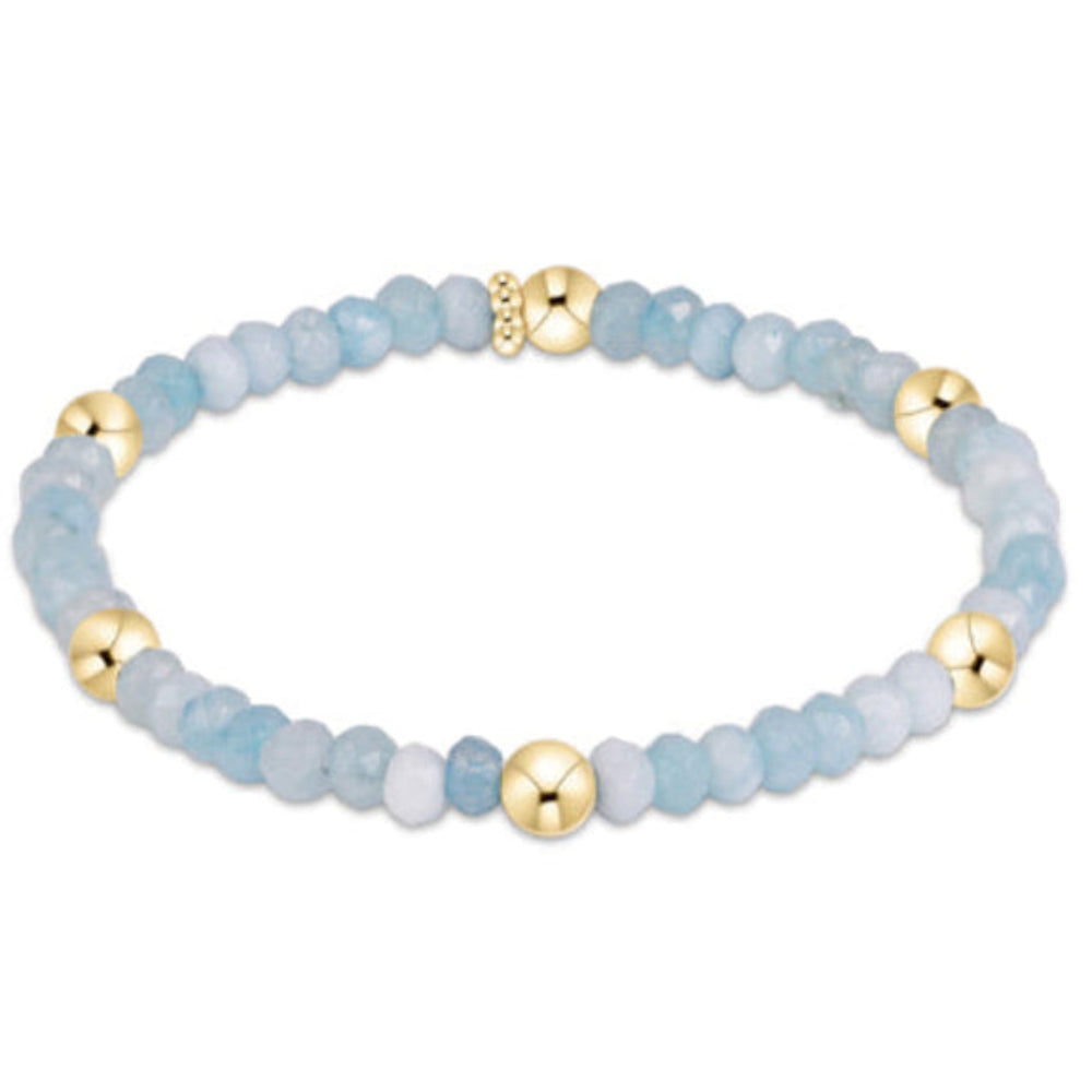 A beaded stretch bracelet featuring light blue and white stone beads with polished gold spacer beads and a gold clasp, shown on a plain white background.