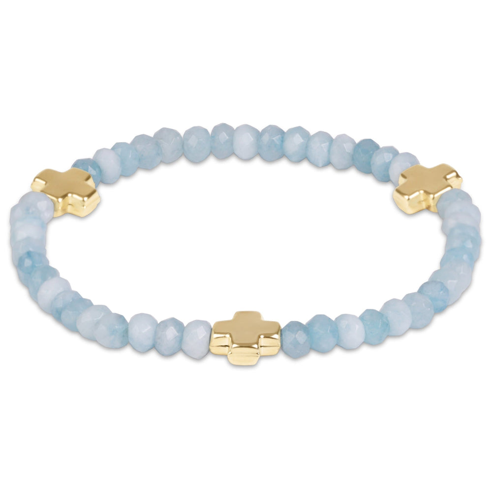 A beaded stretch bracelet featuring light blue faceted beads and four polished gold-tone cross charms, displayed on a clean white background.