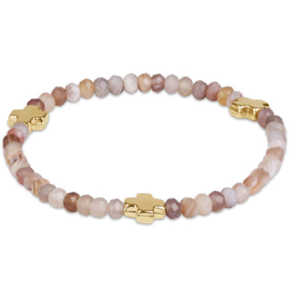 A beaded stretch bracelet featuring faceted stone beads in shades of pink, beige, and brown, accented by three gold-tone cross charms, shown on a plain white background.