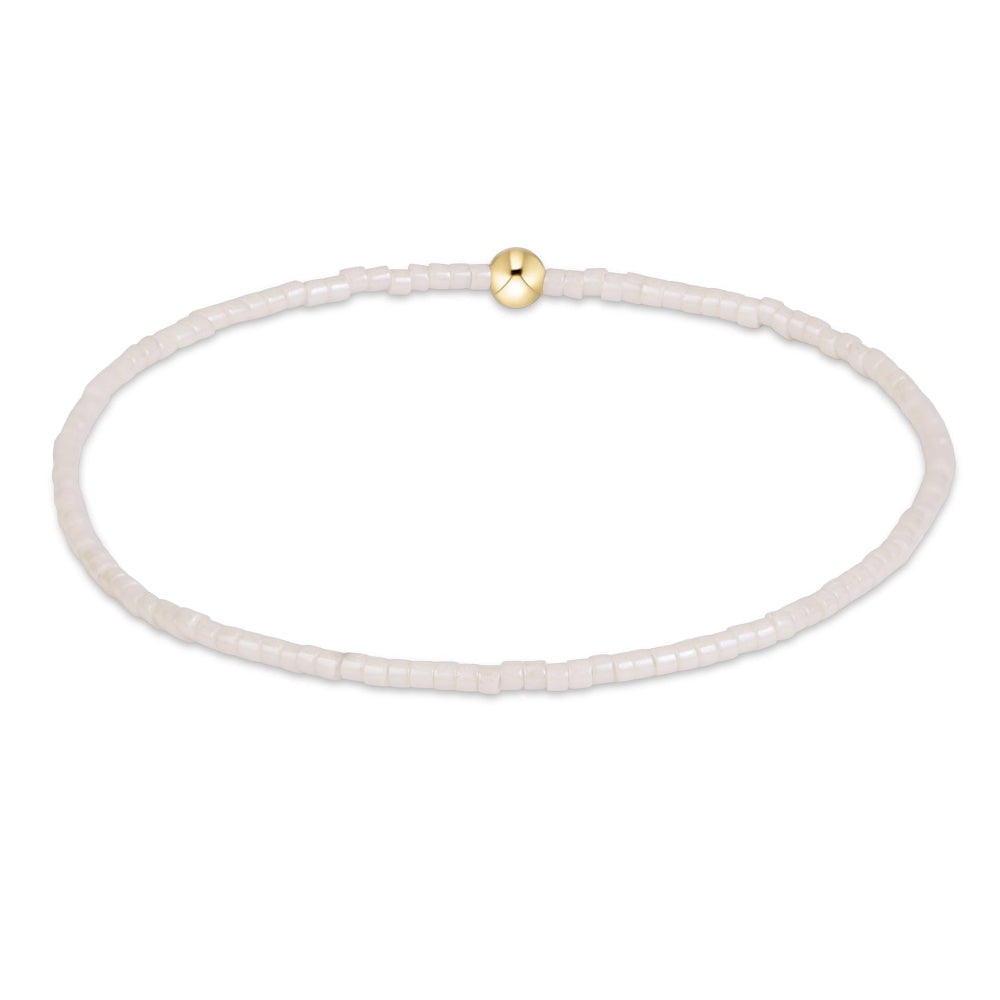 A delicate beaded bracelet made of small translucent white beads with a single polished gold bead accent at the top, shown on a plain white background.