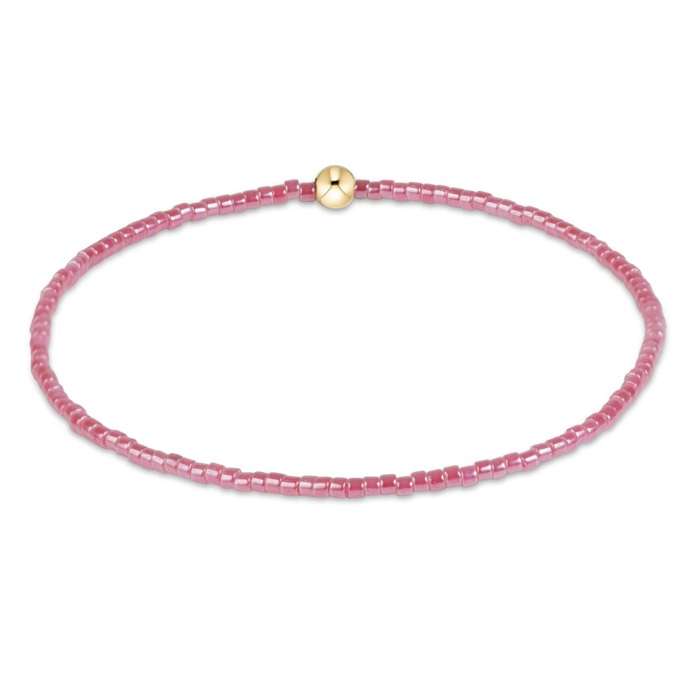 A delicate pink beaded bracelet with a small gold-toned round charm in the center, displayed on a clean white background.
