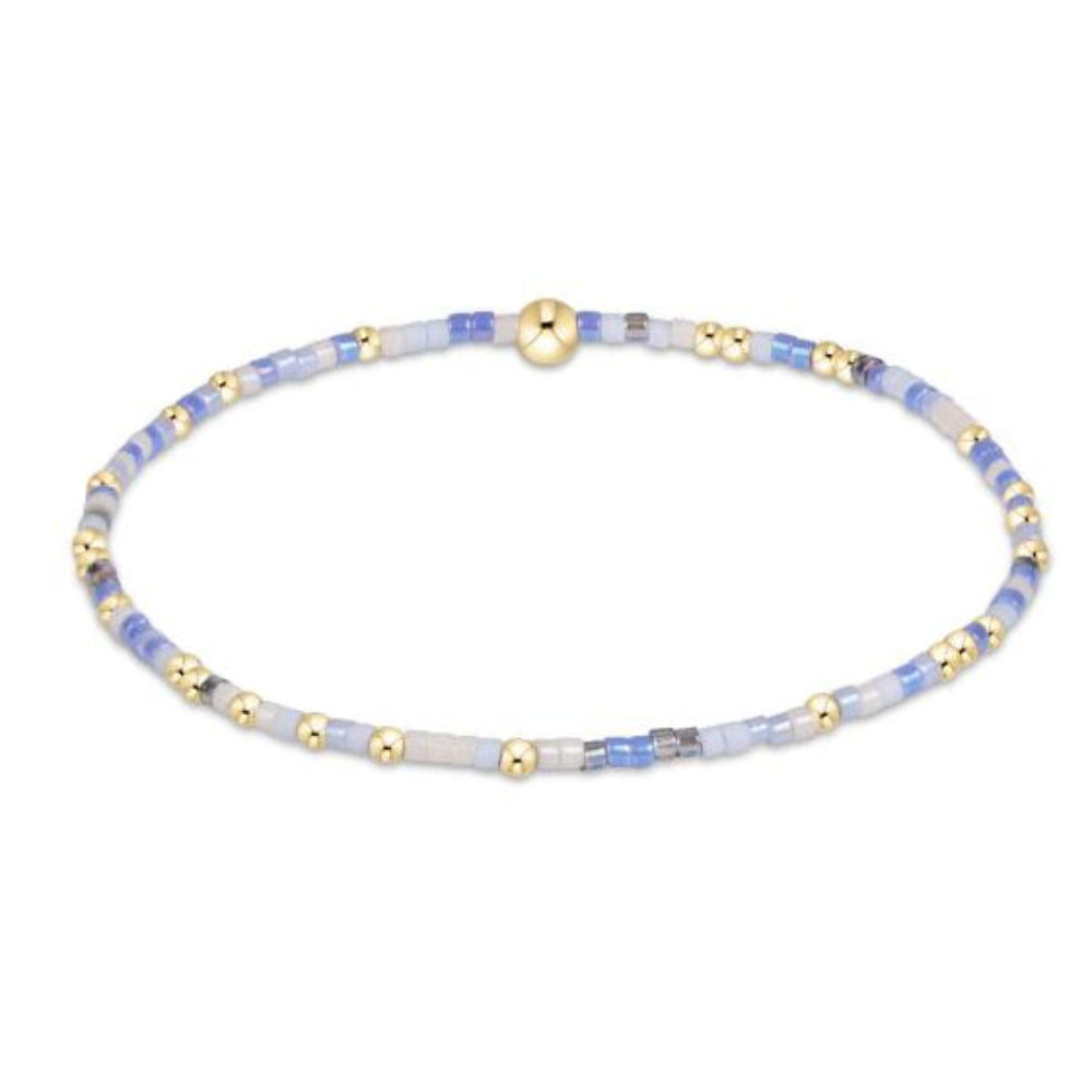 A delicate beaded bracelet with light blue and white beads, accented by small gold spacer beads and a polished gold clasp, shown on a plain white background.