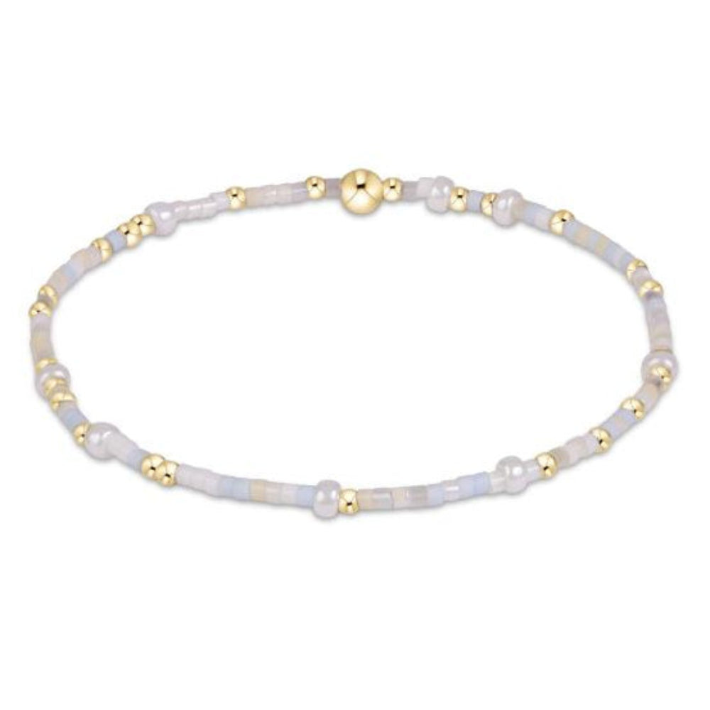 A delicate beaded bracelet featuring pale blue-gray iridescent beads and small polished gold spacer beads, with a larger  gold central bead, shown on a plain white background.