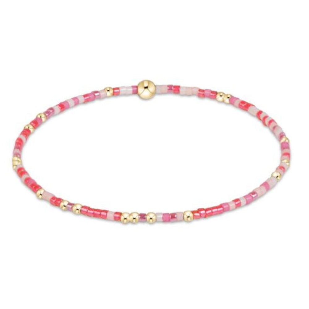 A delicate beaded bracelet with alternating pink and white translucent beads, accented by small gold spacer beads, shown on a plain white background.