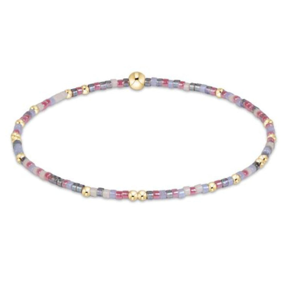 A delicate beaded stretch bracelet featuring translucent lavender and pink beads, gray accents, and polished gold spacer beads on a white background.