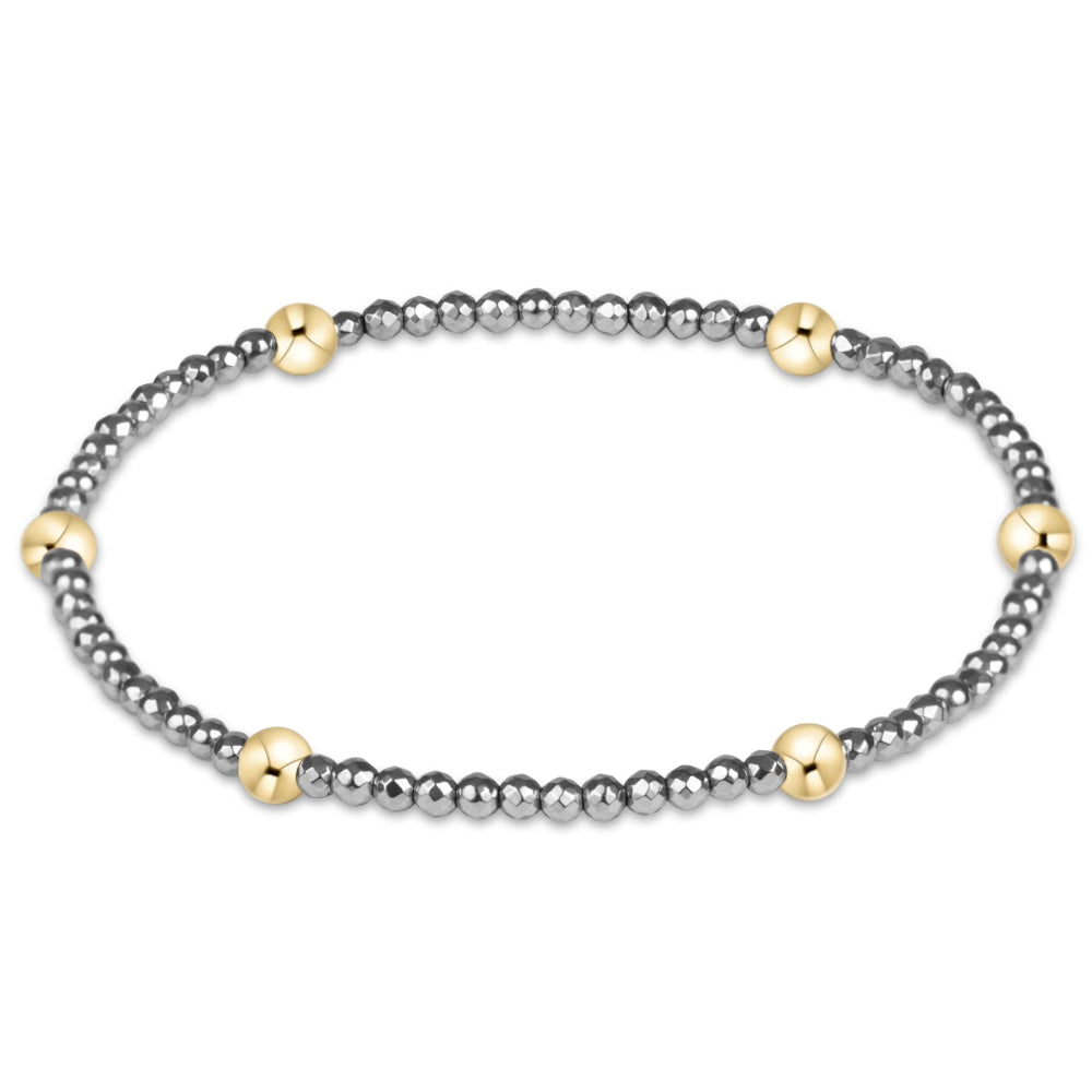 A beaded stretch bracelet featuring small dark gray beads with alternating polished gold-toned round accents, displayed on a clean white background.