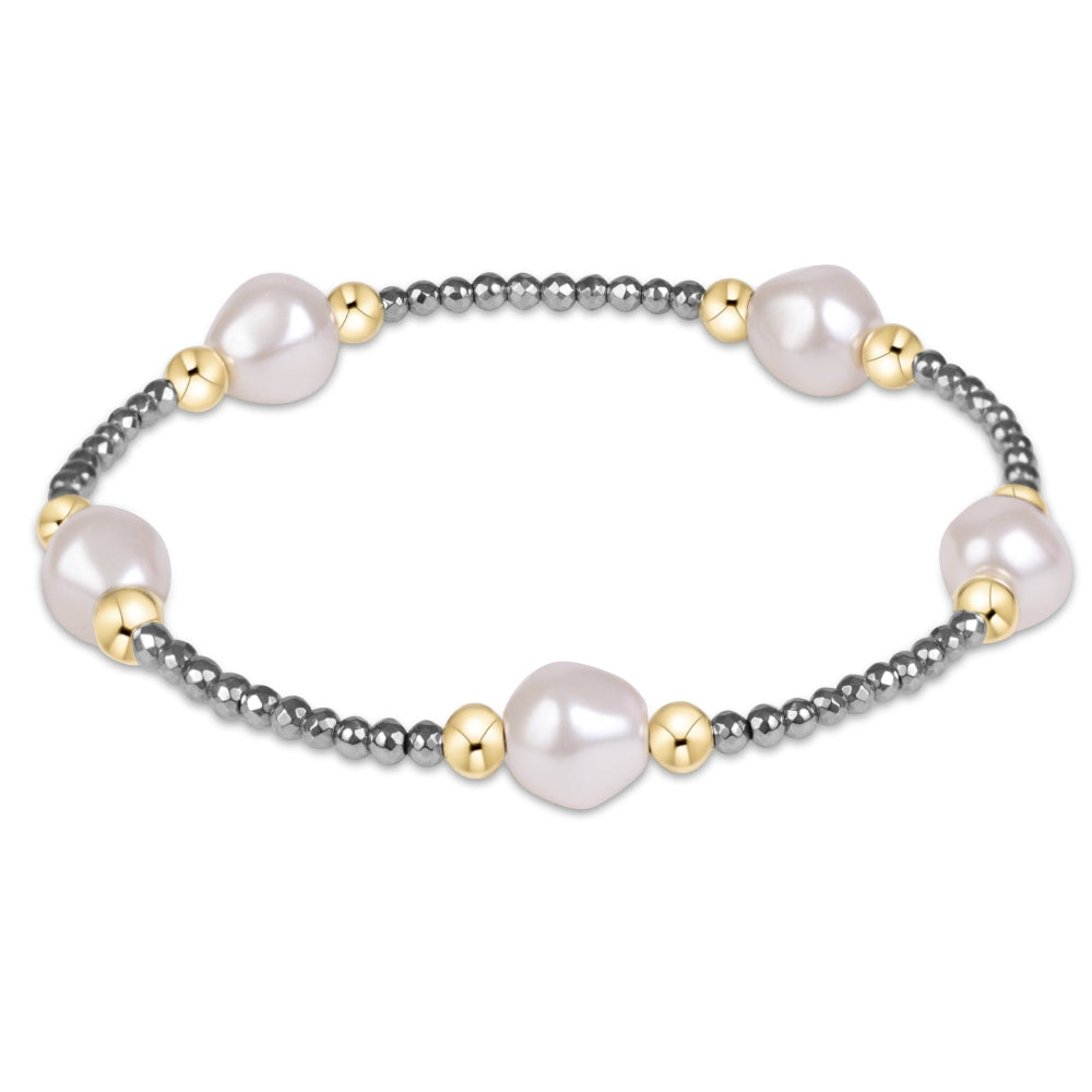 A beaded stretch bracelet featuring large, irregular white freshwater pearls, polished gold-toned spacer beads, and a dark gray metallic beaded chain, shown on a plain white background.