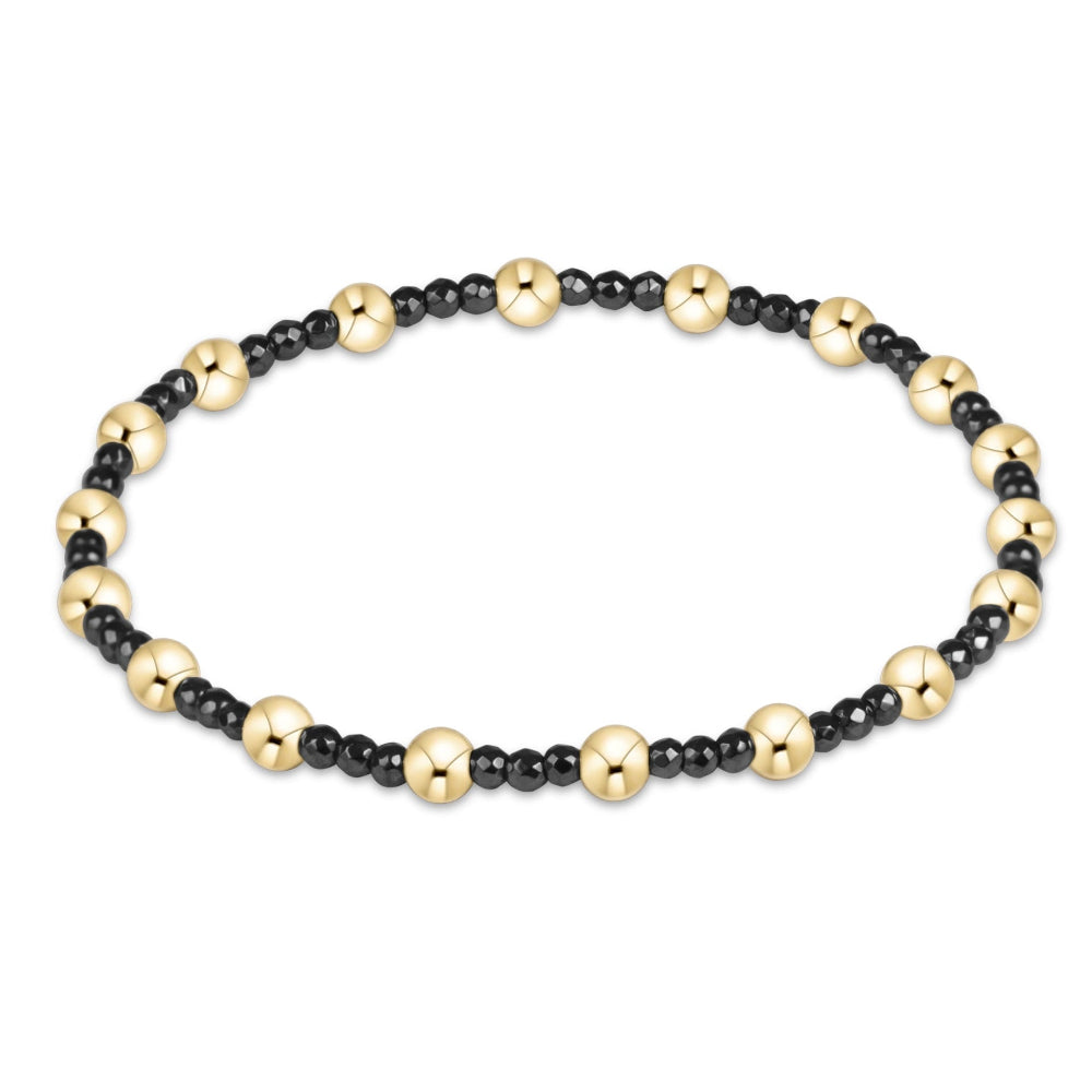 A beaded stretch bracelet featuring alternating polished gold-tone round beads and smaller matte black round beads, displayed on a clean white background.