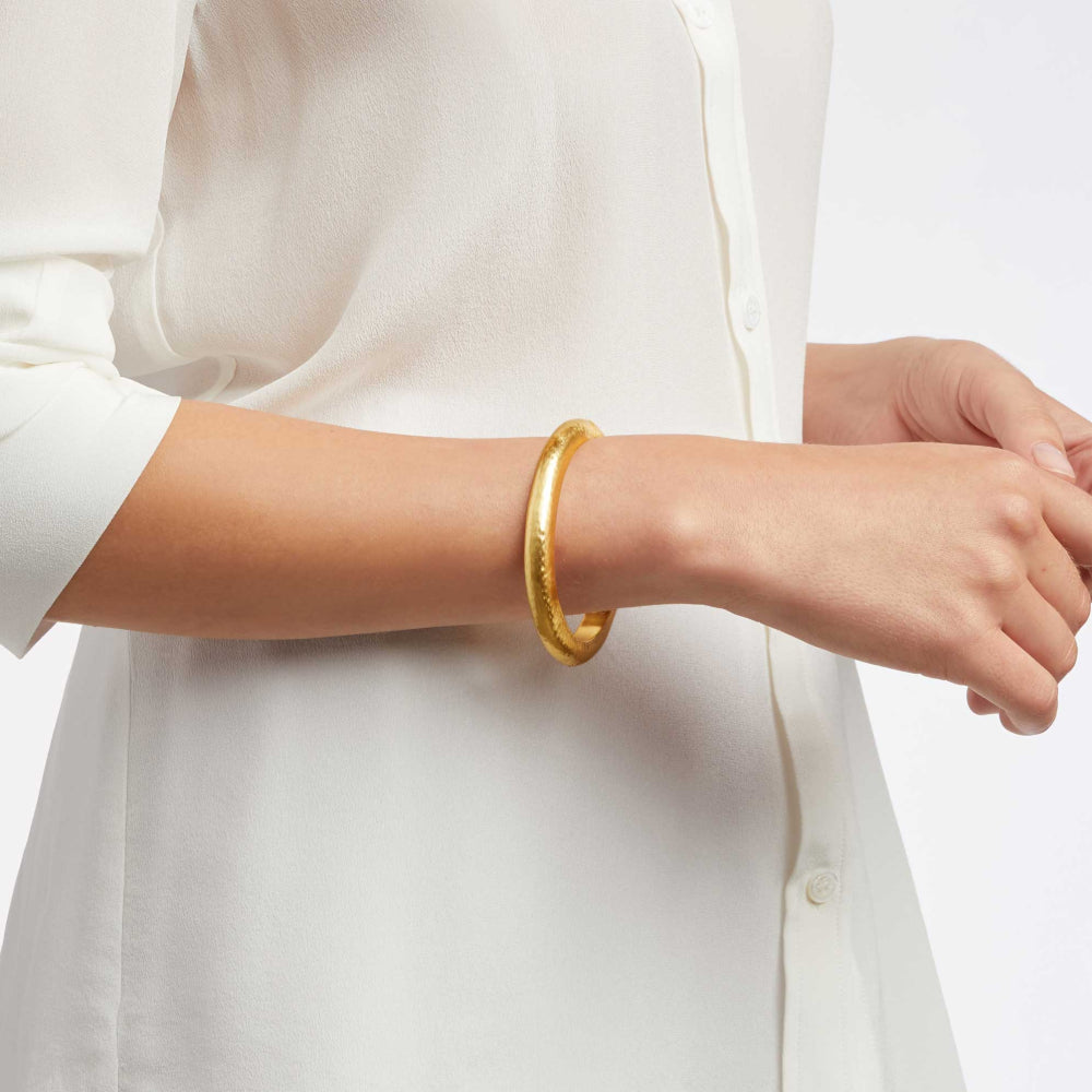 Gold bracelet on a person wearing a white shirt against a light background