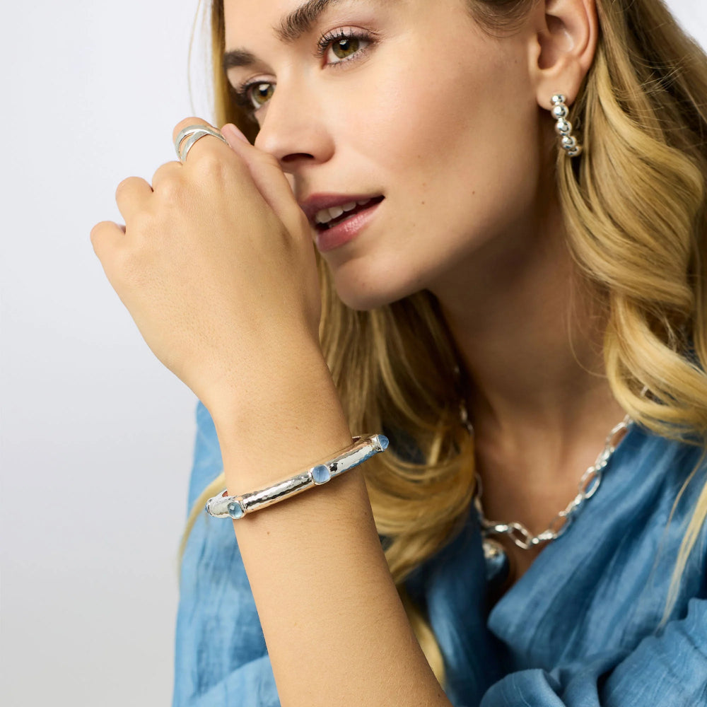 Woman wearing silver jewelry including a bracelet, ring, and earrings on a light background