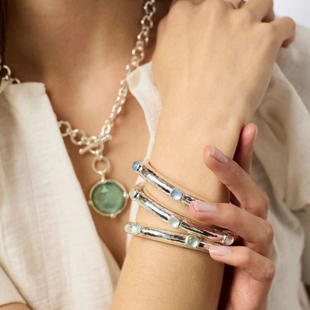 Close-up of a person wearing silver bracelets with gemstones on a neutral background