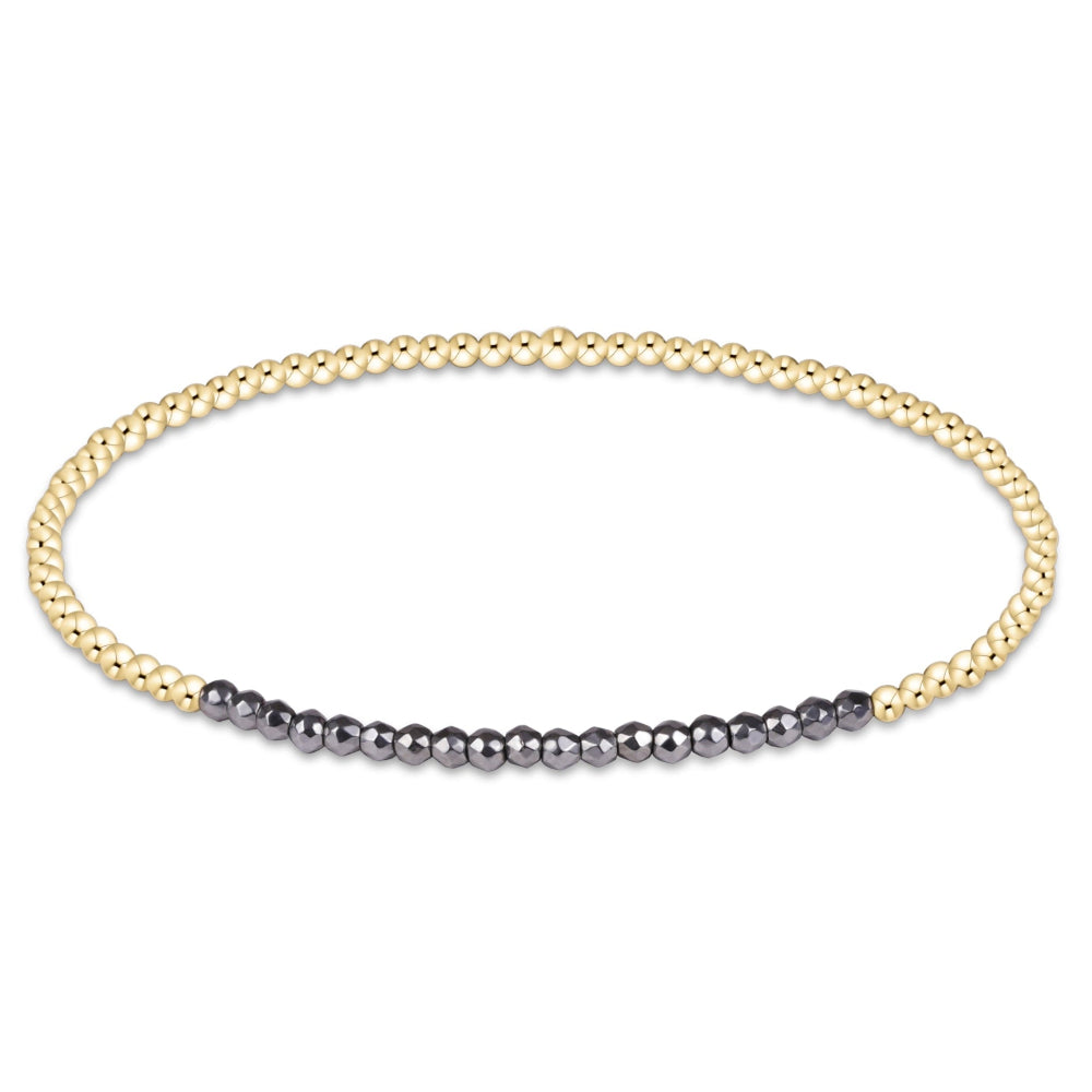 A delicate gold bead bracelet featuring a central segment of small dark gray beads, displayed on a clean white background.