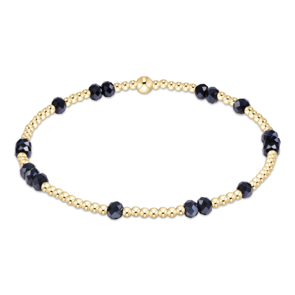 A delicate beaded bracelet featuring alternating gold-toned round beads and dark navy faceted beads, displayed on a clean white background.