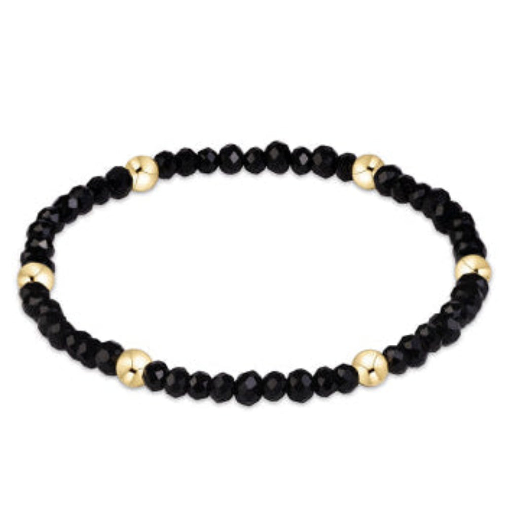 A beaded stretch bracelet featuring faceted black beads and polished gold spacer beads, displayed on a clean white background.