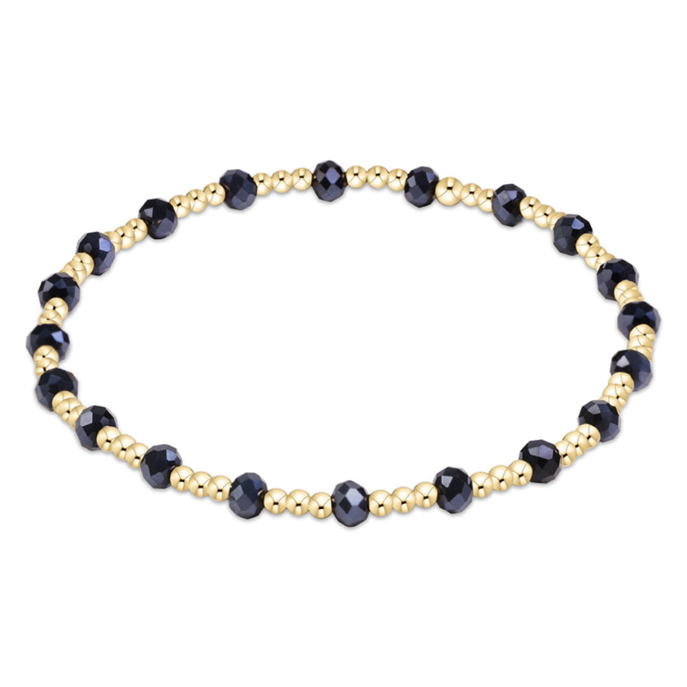 A beaded stretch bracelet featuring faceted dark blue beads and small metallic gold spacer beads, arranged in a circular shape on a plain white background.