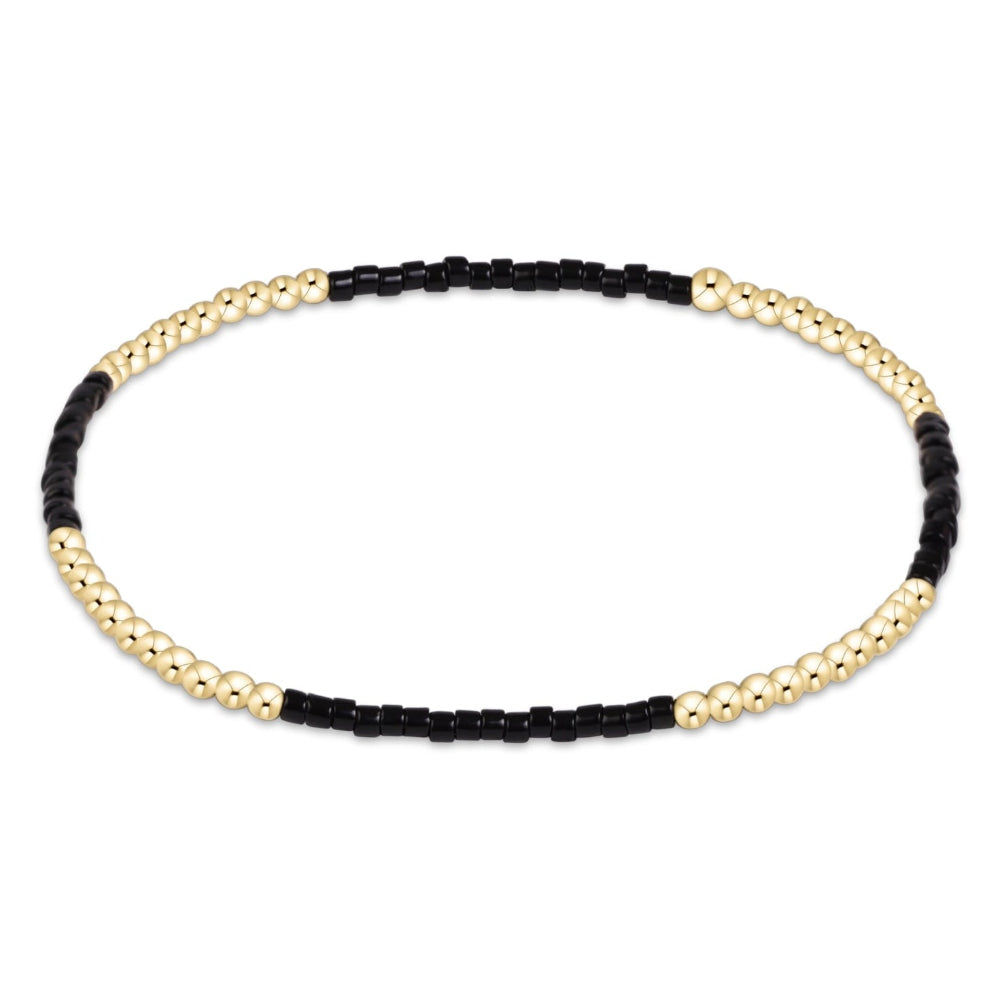A beaded stretch bracelet featuring alternating sections of polished gold-toned round beads and matte black cylindrical beads, displayed on a clean white background.