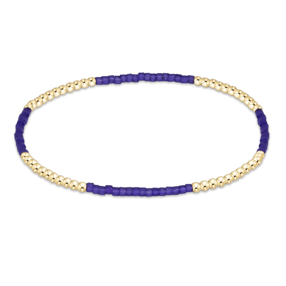 A beaded stretch bracelet featuring alternating strands of small gold-toned beads and dark purple cylindrical beads, displayed on a clean white background.