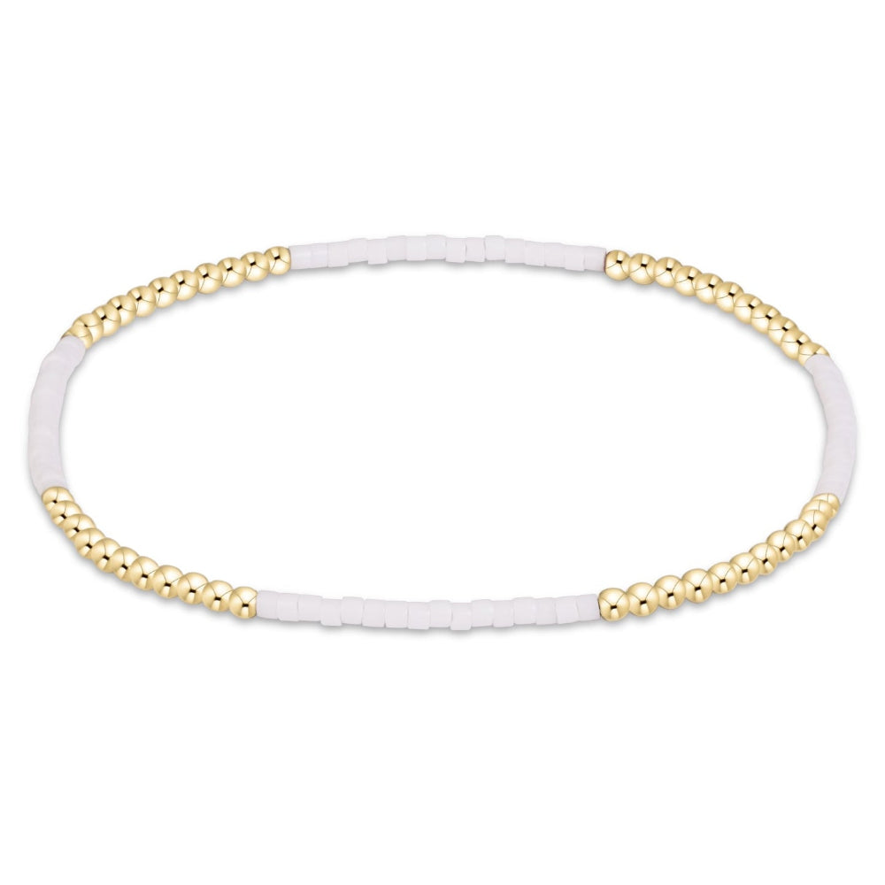 A delicate beaded stretch bracelet featuring alternating strands of small metallic gold beads and matte white cylindrical beads, displayed on a clean white background.