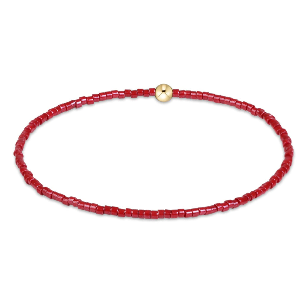 A delicate red beaded bracelet with a small gold clasp, displayed on a clean white background.