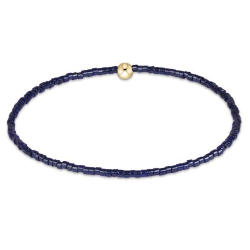 A delicate beaded bracelet made of dark navy blue cylindrical beads, featuring a single polished gold spacer bead at the top, displayed on a clean white background.