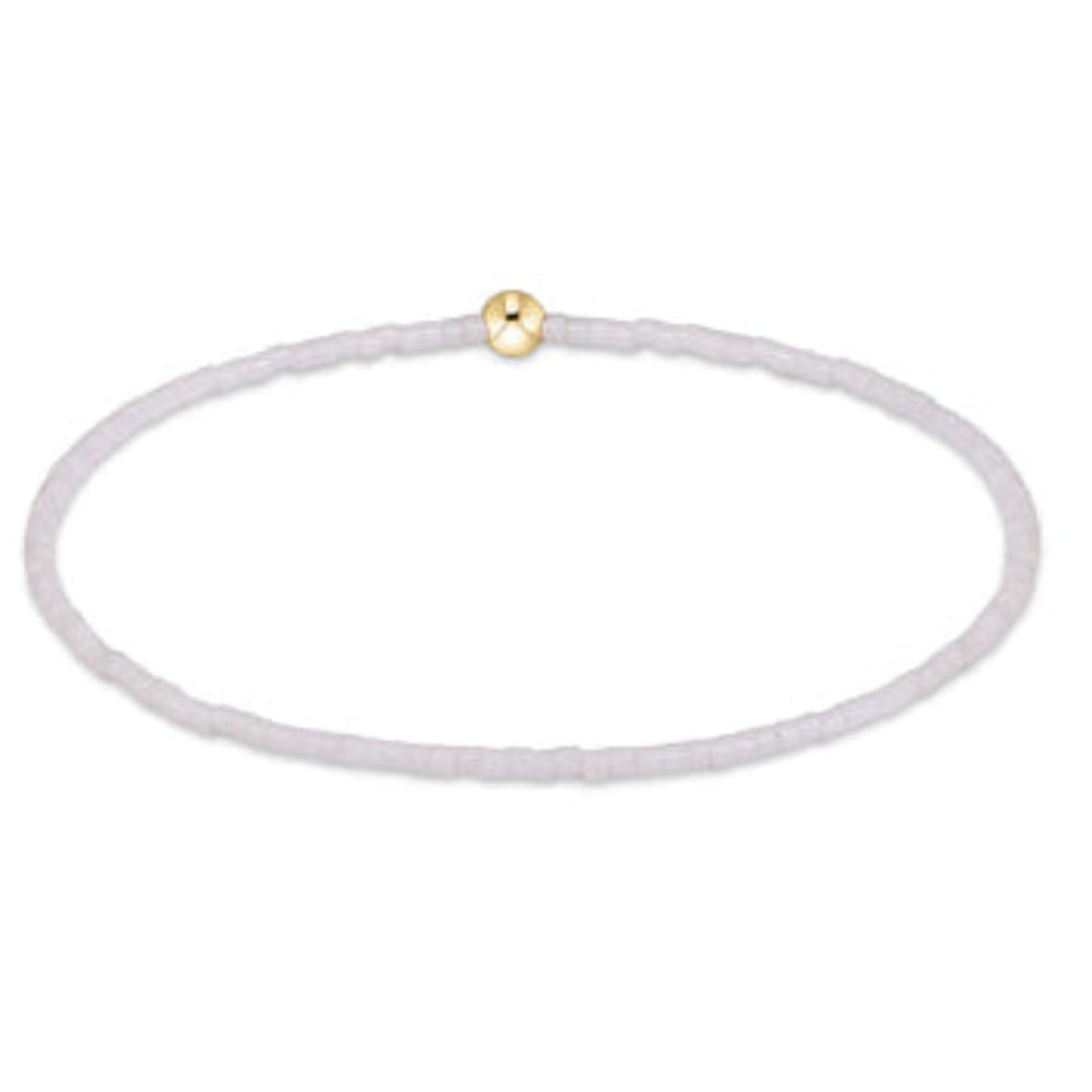 A delicate beaded bracelet with a textured white cord and a small, polished gold bead accent, shown on a plain white background.