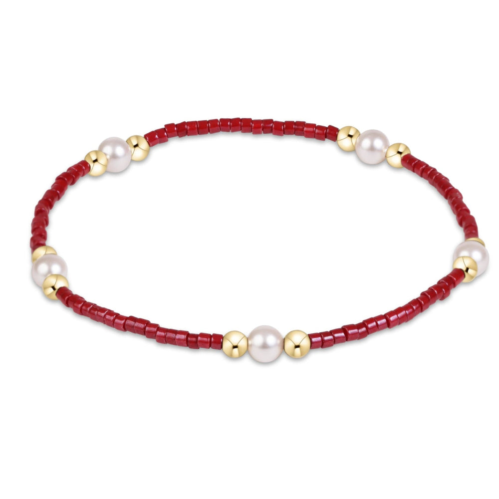 A delicate beaded bracelet featuring a deep red beaded cord accented by white freshwater pearls and small gold spacer beads, shown on a plain white background.