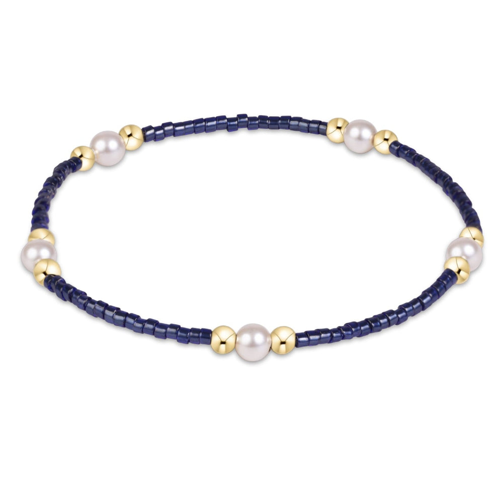 A beaded stretch bracelet featuring dark navy blue faceted beads, white freshwater pearls, and polished gold spacer beads, displayed on a clean white background.
