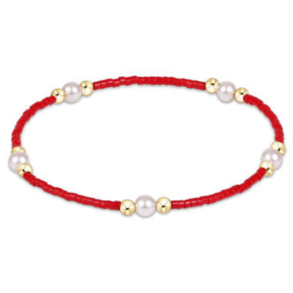 A delicate red beaded bracelet with small white pearls and gold spacer beads, displayed on a clean white background.