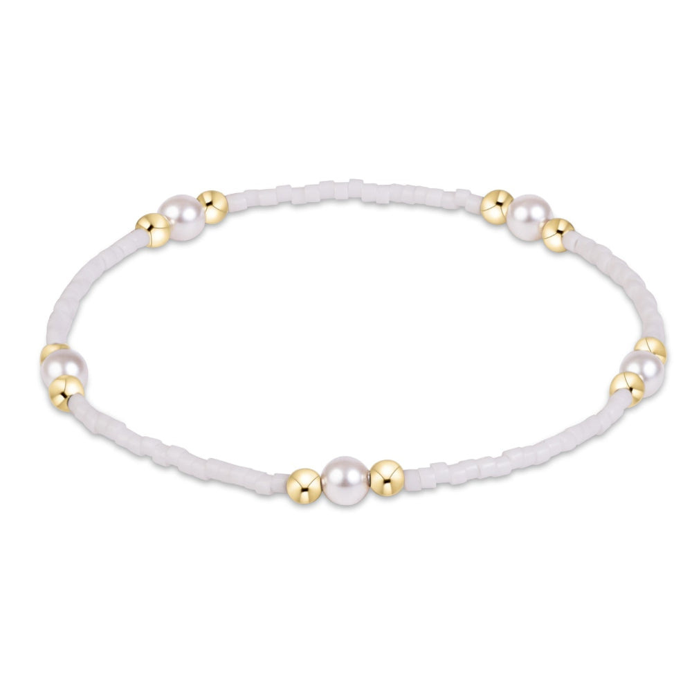 A delicate beaded bracelet featuring white textured beads, white pearls, and polished gold spacer beads, arranged in a circle on a plain white background.