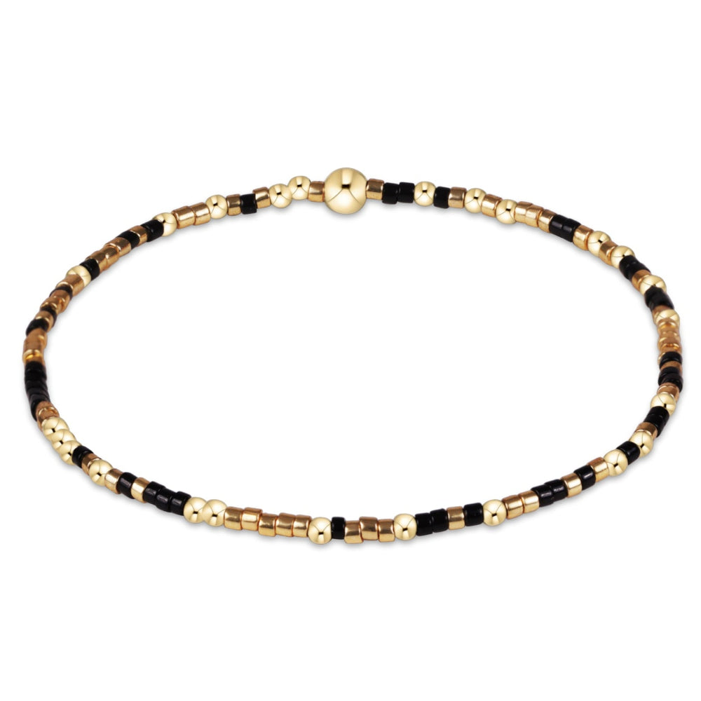 A delicate beaded bracelet with alternating black and gold metallic beads, featuring a small gold bead, shown on a plain white background.