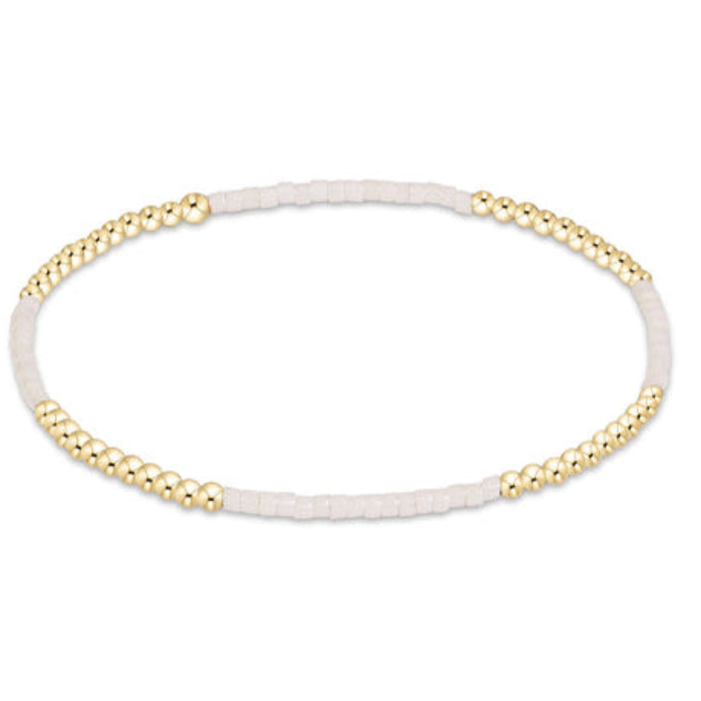 A delicate bangle bracelet featuring a white textured band accented by gold-toned beaded segments on each side, shown against a plain white background.