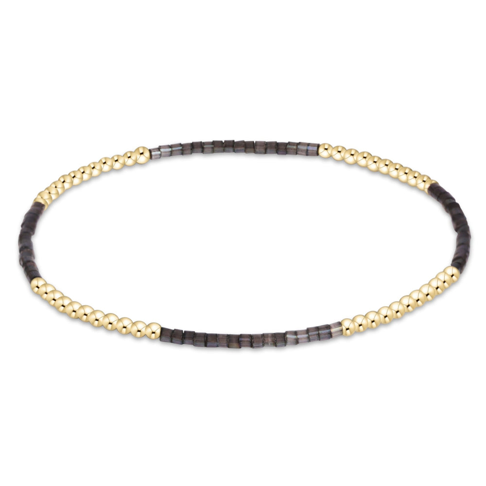 A delicate beaded stretch bracelet featuring alternating sections of textured gold beads and small dark gray faceted beads, displayed on a clean white background.