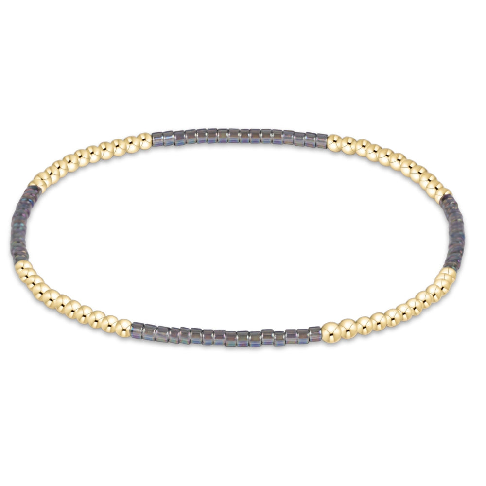 A delicate chain bracelet featuring alternating sections of textured gold and dark gray metal, displayed on a clean white background.