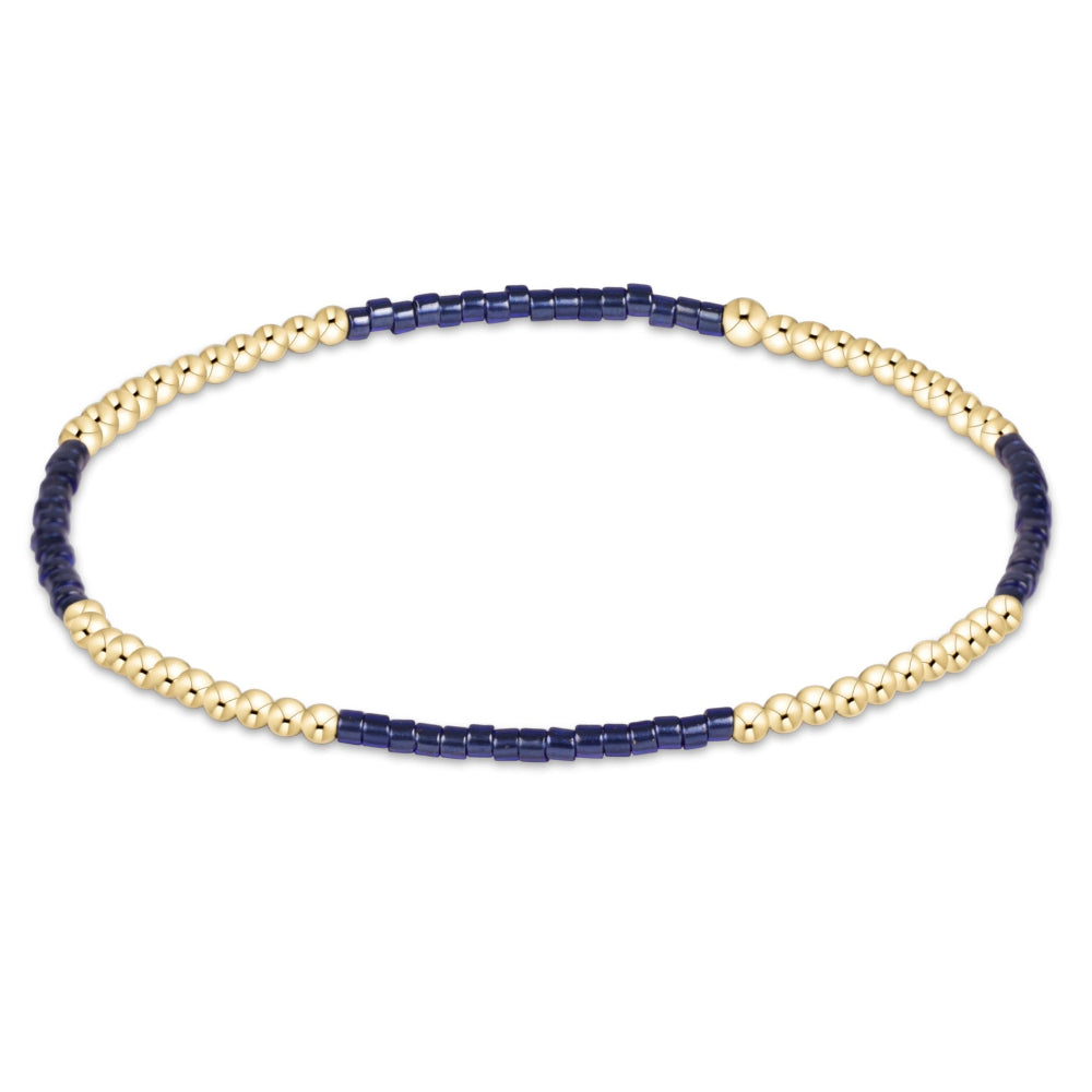 A delicate beaded bracelet featuring alternating sections of dark navy blue beads and textured gold-toned beads, displayed on a clean white background.