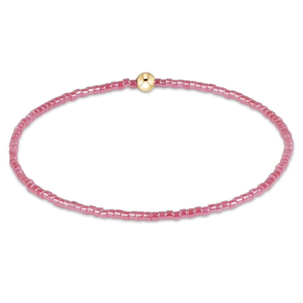 A delicate pink beaded bracelet with a small gold-toned round bead accent, displayed on a clean white background.