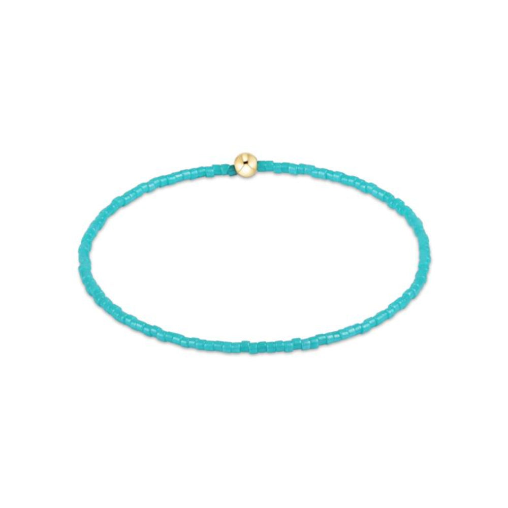 Turquoise beaded bracelet with a gold bead on a white background