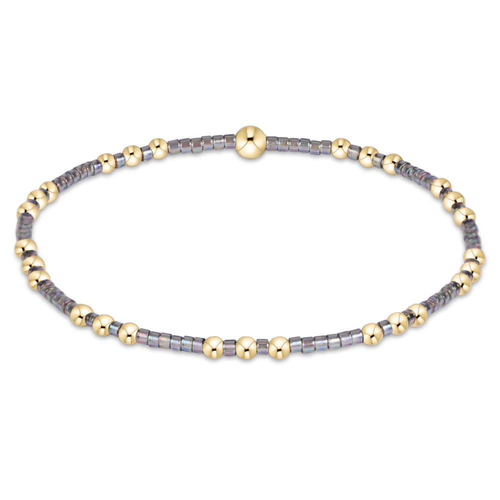 A delicate beaded bracelet featuring alternating strands of small gray beads and polished gold-tone spacer beads, with a central gold bead, shown on a plain white background.