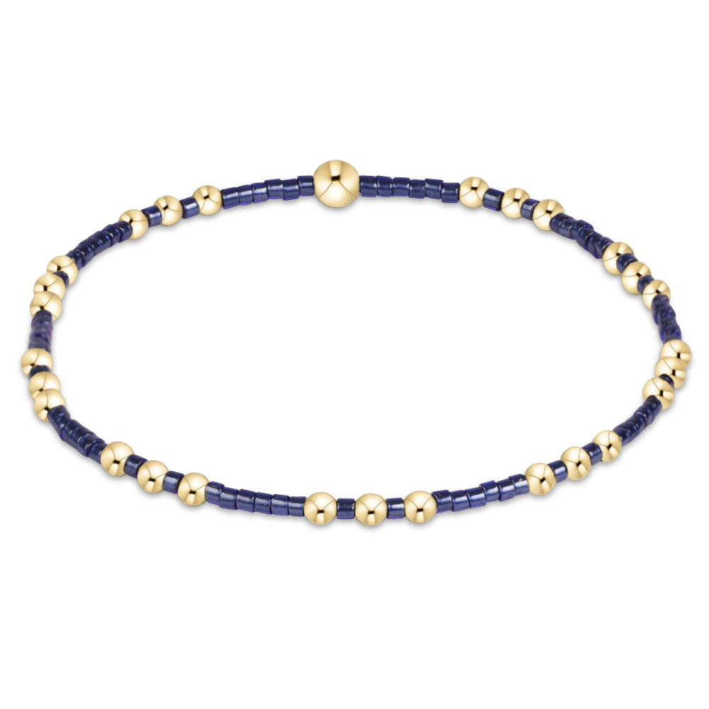 A delicate beaded bracelet featuring dark navy blue beads alternating with small metallic gold beads, shown on a plain white background.