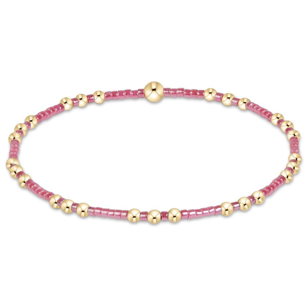 A delicate beaded stretch bracelet featuring alternating rows of small pink faceted beads and polished gold-tone round beads, with a central gold bead, shown on a plain white background.