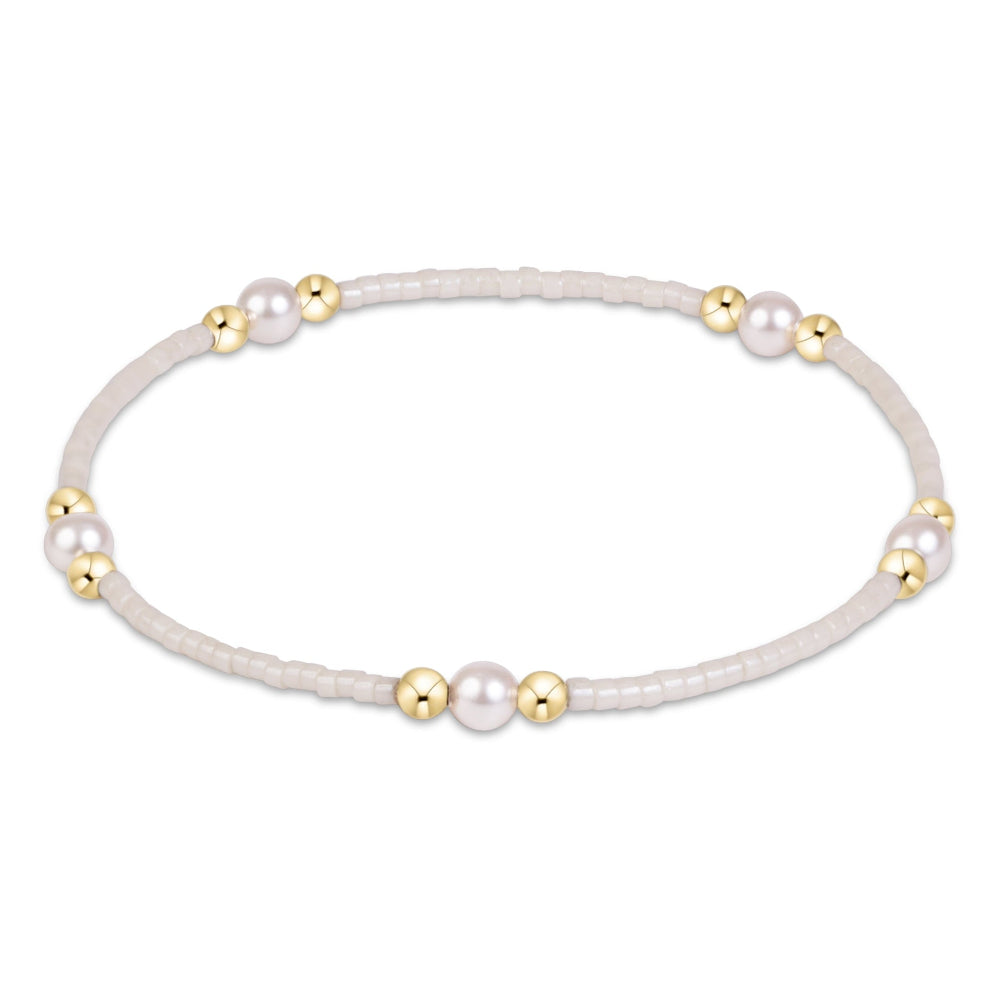 A delicate beaded bracelet with white faux pearls and small gold spacer beads, displayed on a clean white background.