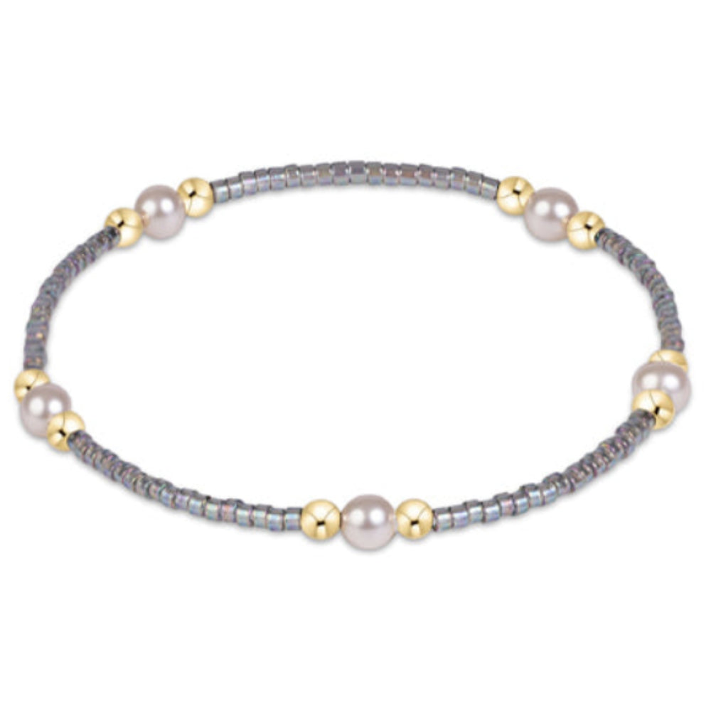 A delicate beaded bracelet featuring gray seed beads, white pearls, and small gold spacer beads, displayed on a clean white background.