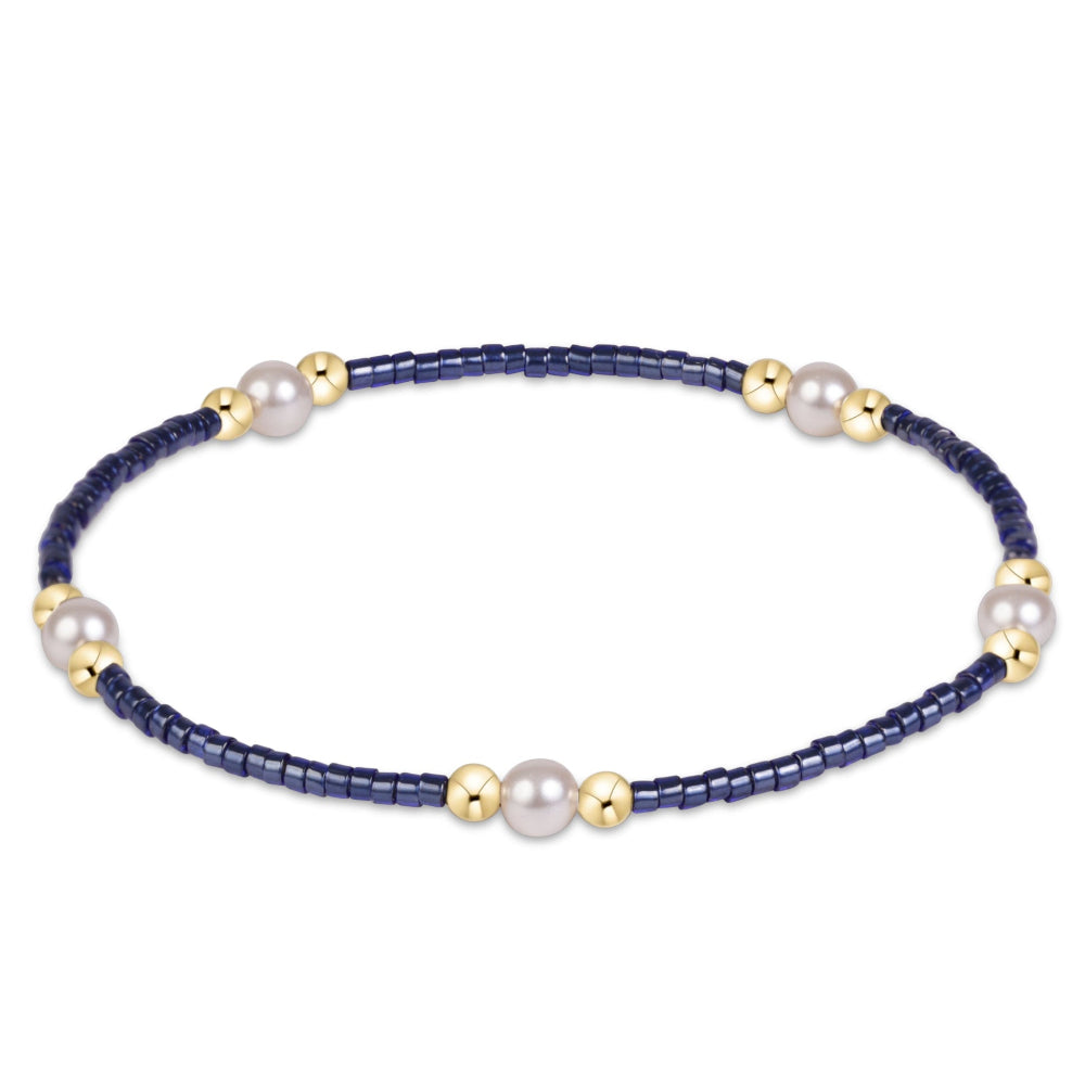 A delicate beaded bracelet featuring dark navy blue seed beads, accented with small gold spacers and white freshwater pearls, displayed on a clean white background.
