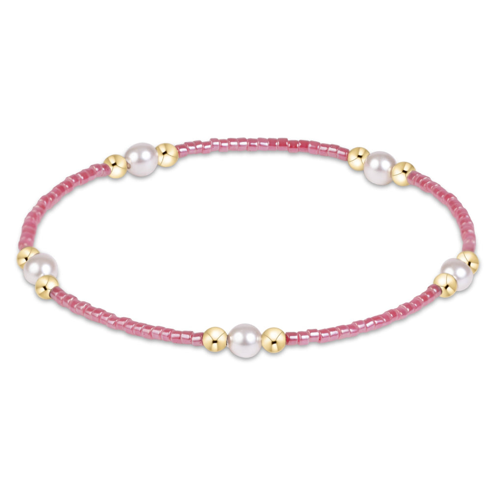 A delicate pink beaded bracelet with white faux pearls and small gold spacer beads, displayed on a clean white background.