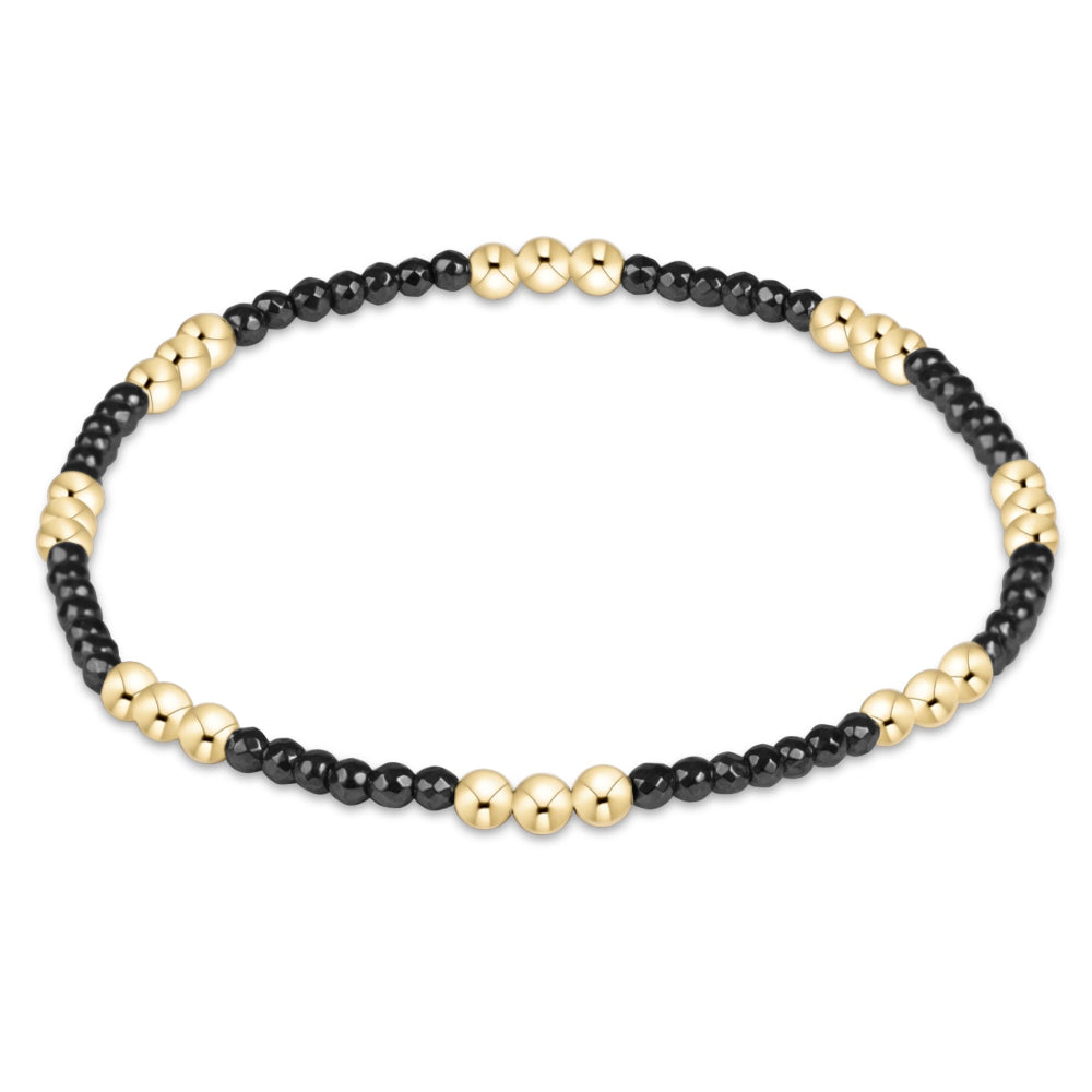 A beaded stretch bracelet featuring alternating sections of small black beads and polished gold-tone beads, displayed on a clean white background.