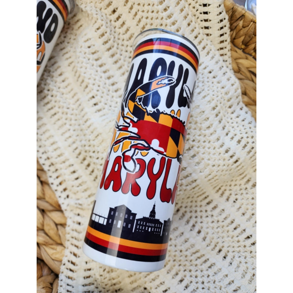 Colorful tumbler with 'Maryland Crab' design on in a basket on a white blanket 