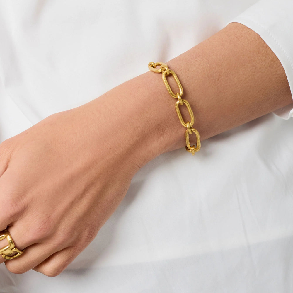 Gold chain bracelet on a wrist with a plain background