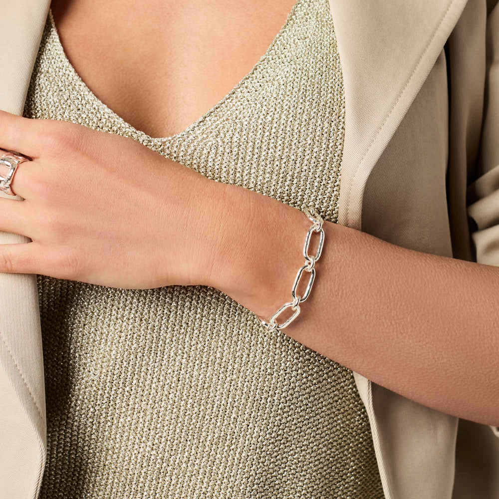 Close-up of a person wearing a silver chain bracelet on a neutral background