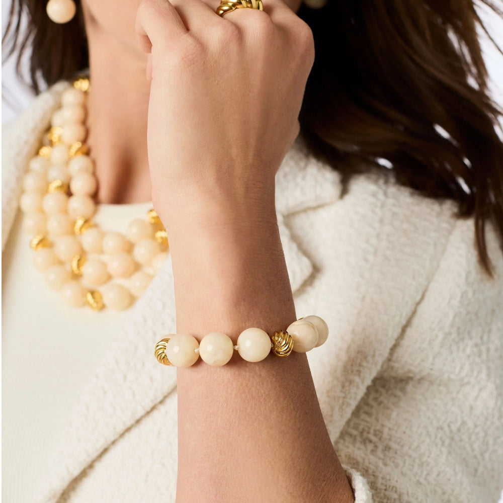Close-up of a person's wrist wearing a beige beaded bracelet with gold accents, against a neutral background.