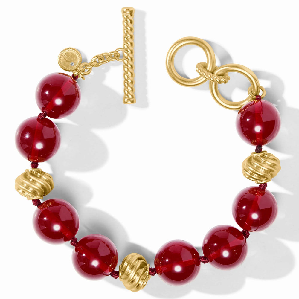 A beaded bracelet with glossy red faceted beads, textured gold spacer beads, and a gold toggle clasp on a white background.